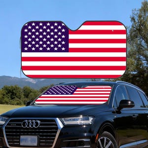 May include: Car sunshade displaying the American flag. The sunshade has a red, white, and blue design, with the stars and stripes of the US flag. It is fitted to the windscreen of a black car, offering protection from sunlight.