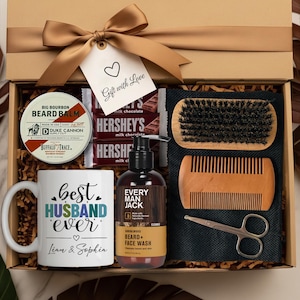 May include: A gift box with a gold bow, containing a mug that says "Best Husband Ever", beard balm, beard wash, a beard brush, comb, scissors, and Hershey's chocolate bars. The tag says "Gift with Love".