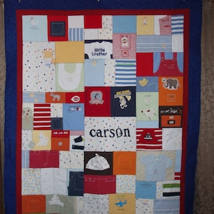 May include: A blue and red patchwork quilt with a variety of baby clothes sewn together. The quilt has a blue border and the name "carson" is written in the center.