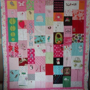May include: A pink and white patchwork quilt with a variety of fabrics and patterns. The quilt is made up of squares and rectangles, and it features a variety of colors, including pink, white, blue, green, and red. The quilt is decorated with a variety of designs, including flowers, polka dots, stripes, and animals. The quilt is also personalized with the name "Sophia".