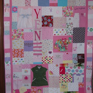 May include: A pink baby quilt with a variety of colorful fabric squares. The quilt is made up of baby clothes and features the name "YEN" in large pink letters. The quilt also includes the phrase "Life is good."