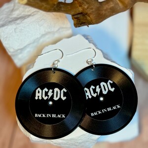 May include: A pair of black earrings shaped like vinyl records with the text "AC/DC Back in Black" in silver glitter.