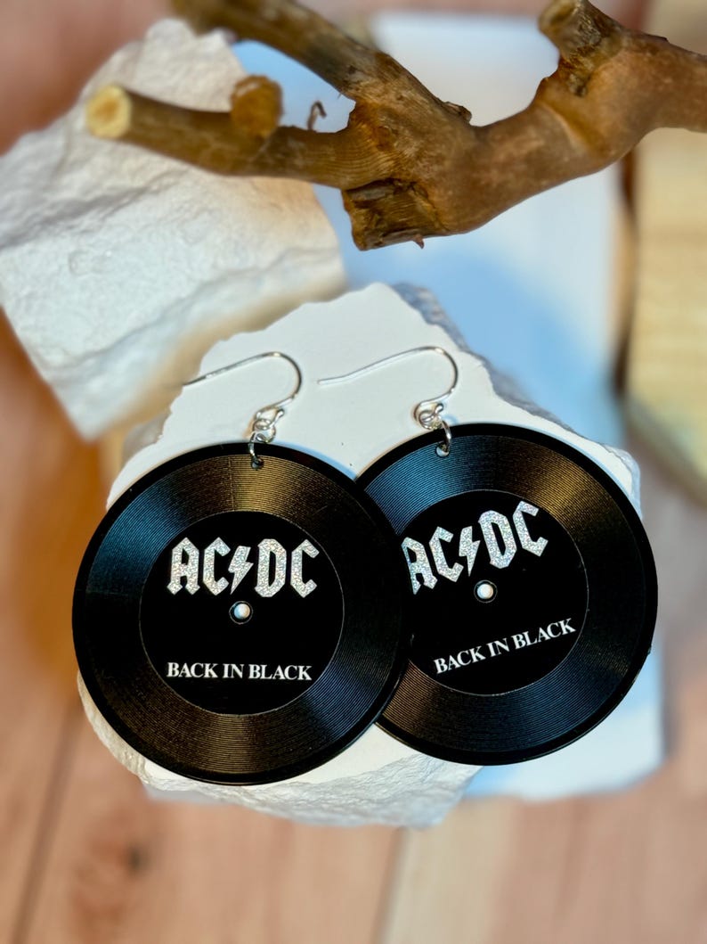 May include: A pair of black earrings shaped like vinyl records with the text "AC/DC Back in Black" in silver glitter.