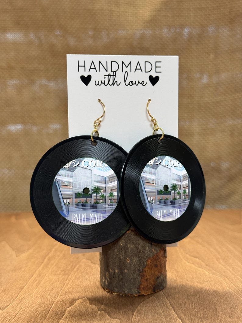 May include: A pair of black vinyl record earrings with a picture of the Palm Mall shopping center. The earrings are handmade and have gold hooks. The card behind the earrings says "Handmade with love."