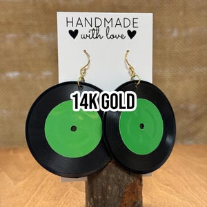 May include: A pair of black and green record earrings with gold hooks. The earrings are handmade and feature the text "14K GOLD".