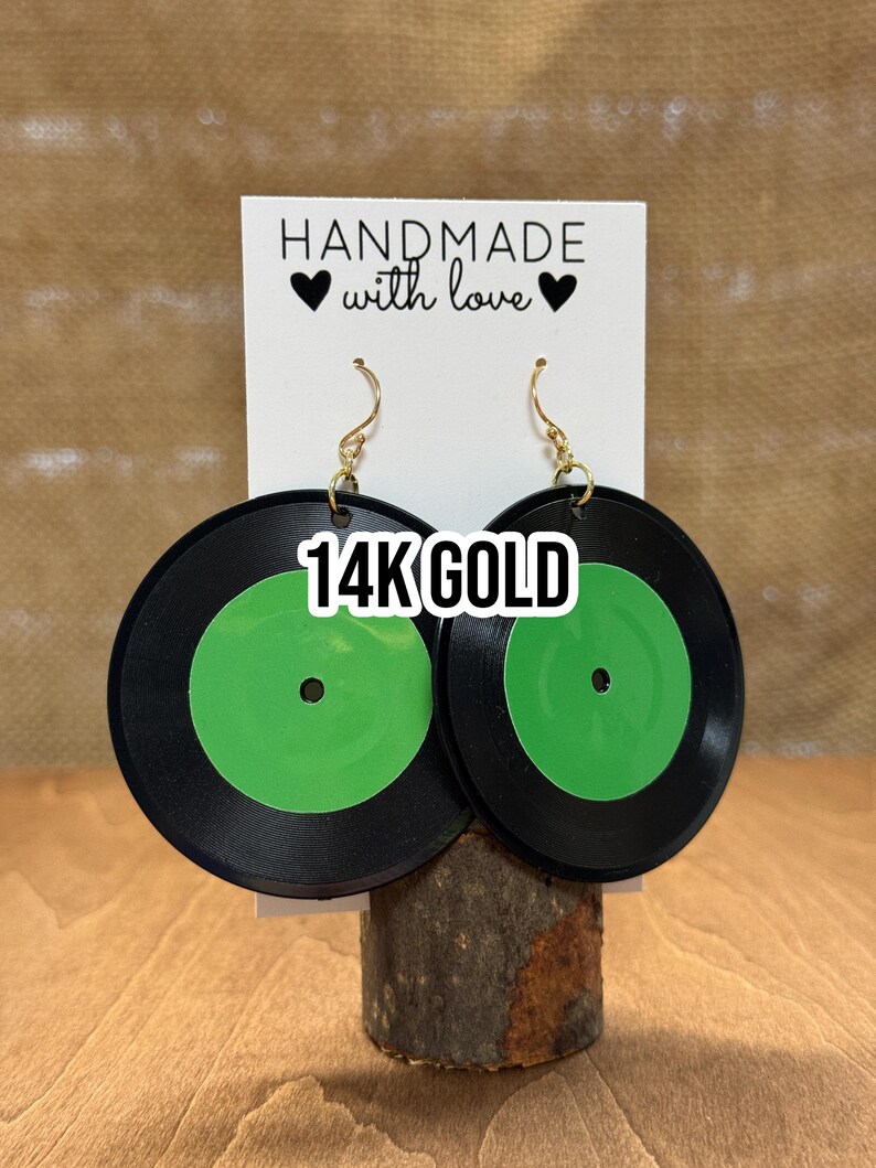 May include: A pair of black and green record earrings with gold hooks. The earrings are handmade and feature the text "14K GOLD".