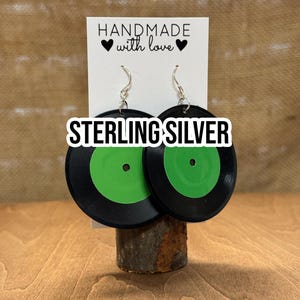 May include: Sterling silver earrings shaped like a black vinyl record with a green label. The earrings are handmade with love.
