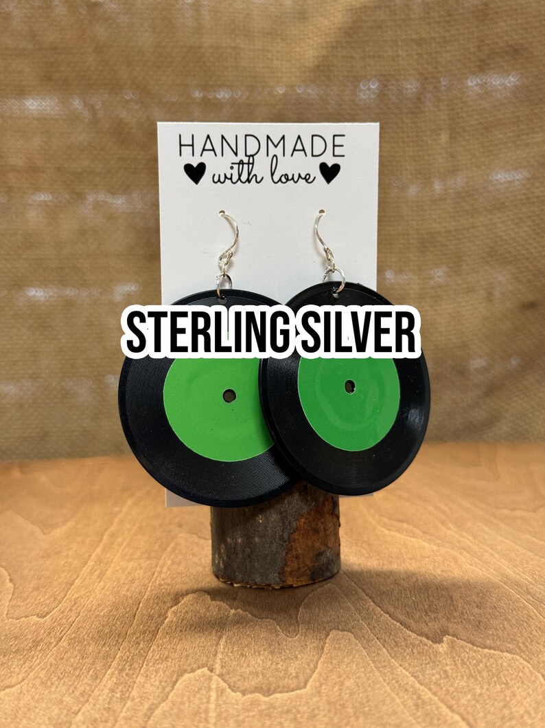 May include: Sterling silver earrings shaped like a black vinyl record with a green label. The earrings are handmade with love.