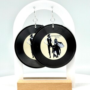 May include: A pair of black vinyl earrings featuring the Fleetwood Mac "Rumours" album cover. The earrings are hanging from silver hooks.