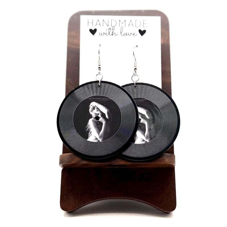 May include: A pair of black and white earrings with a photo of a woman on each earring. The earrings are hanging from a wooden stand with the text "HANDMADE with love" on it.