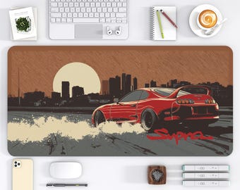 May include: A red sports car desk mat with a cityscape and sunset design. The mat features a red car with the word "Supra" in a stylized font. The mat measures 16 x 32 inches.