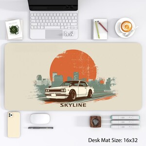 May include: A beige desk mat featuring a white vintage car driving on a road, with a large orange sun in the background and a cityscape. The word "SKYLINE" is printed below the car. The desk mat measures 16 x 32 inches.