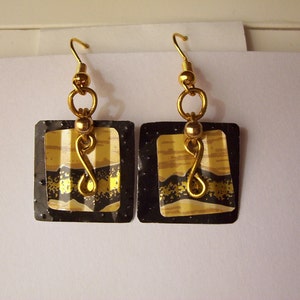 May include: A pair of gold and black square earrings with a gold wire design. The earrings have a gold hook closure.