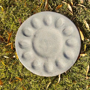 Peut inclure: Une assiette ronde en céramique grise mouchetée avec une série d'indentations incurvées sur le bord. L'assiette est posée sur de l'herbe verte et des feuilles mortes.