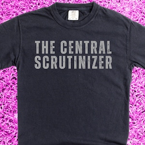 Puede incluir: Una camiseta azul oscuro con el texto "The Central Scrutinizer" impreso en blanco en la parte delantera.