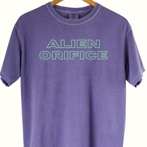 T-shirt met tekst van Zappa. Alien Orifice wordt geleverd op een premium, Clothing-dye T-shirt met zachte, vintage vervaging. FZ-komedie goud.