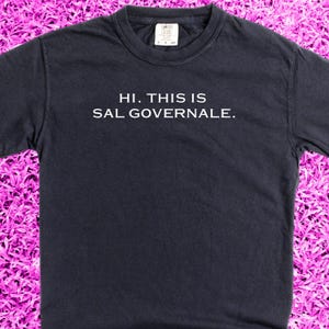 May include: A dark navy blue t-shirt with white text that reads "HI. THIS IS SAL GOVERNALE."