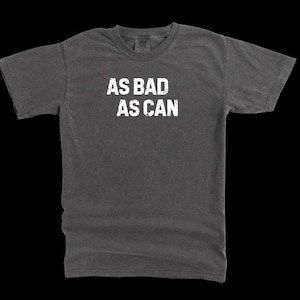 Puede incluir: Una camiseta gris oscuro con el texto "AS BAD AS CAN" impreso en blanco en la parte delantera.