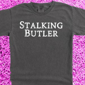 May include: A dark gray t-shirt with the text "STALKING BUTLER" printed in white.