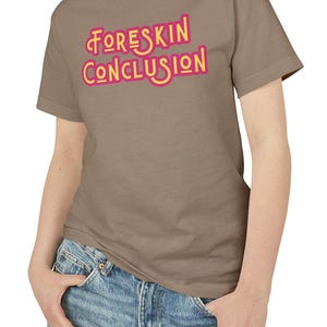 May include: A brown t-shirt with the text "Foreskin Conclusion" in pink and yellow letters.