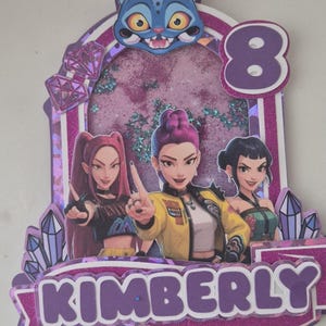 Peut inclure: Décoration de gâteau d'anniversaire violette et rose avec trois personnages de dessins animés, le chiffre 8 et le nom "KIMBERLY". Comprend un visage de chat bleu, des paillettes et des accents de pierres précieuses. Les personnages portent diverses tenues.