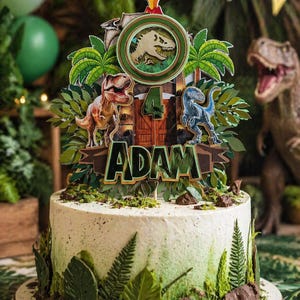 Può includere: Una torta decorata a tema dinosauri. La torta bianca ha dettagli verdi ed è adornata da un topper personalizzato con dinosauri, il numero 4 e il nome "ADAM". La torta è decorata con felci e poggia su una base di legno.