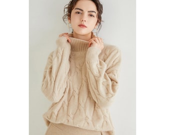 Puede incluir: Un suéter de punto de cable beige con cuello alto. El suéter tiene un corte holgado y está hecho de un material suave y cómodo.