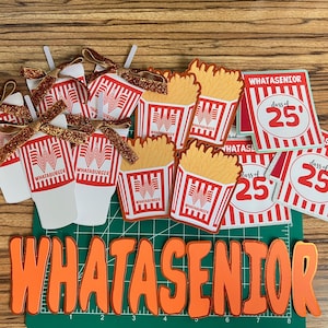Puede incluir: Una colecci&oacute;n de decoraciones de graduaci&oacute;n con tem&aacute;tica de Whataburger. Incluye recortes de papel de papas fritas, vasos de bebidas y tarjetas con el texto "Class of 25". La palabra "WHATASENIOR" se muestra en letras naranjas.