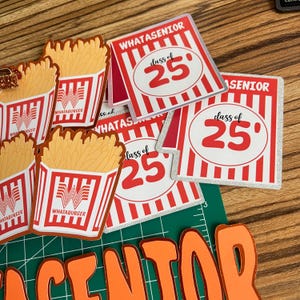 Puede incluir: Una colecci&oacute;n de decoraciones de graduaci&oacute;n con tem&aacute;tica Whataburger. Incluye recortes de papas fritas y tarjetas cuadradas con el texto "WHATASENIOR" y "class of 25" en rojo y blanco. El fondo es una superficie de madera.