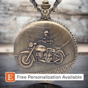 May include: A gold-toned pocket watch with a detailed design of a motorcycle rider on the front. The watch has a chain attached to the top.