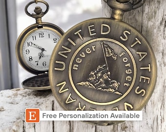 May include: A gold-toned pocket watch with a white face and black hands. The back of the watch features an image of soldiers raising a flag on a hill with the text "United States Marine Corps Never Forget".