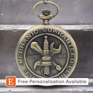 May include: A gold-toned pocket watch with a round face featuring a stylized image of a spark plug, wrench, and screwdriver. The watch face reads "Mechanic Guaranteed Performance" with the words "Super Tuned" printed below the image.