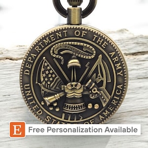 May include: A gold-toned pocket watch with a detailed design featuring the United States Army seal. The seal includes the words "Department of the Army", "United States of America", and "1775".