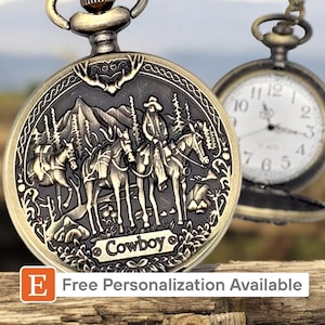 May include: A gold pocket watch with a detailed design of cowboys riding horses in a western landscape. The watch face is white with black Roman numeral hour markers and black hands. The watch has a chain attached to it.