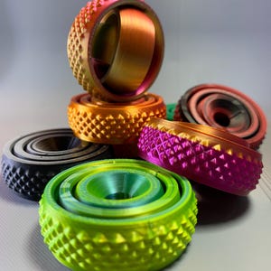 May include: A collection of colorful, 3D printed, geometric shapes with a textured surface. The shapes are stacked on top of each other and are made of different colors, including orange, pink, green, and black.