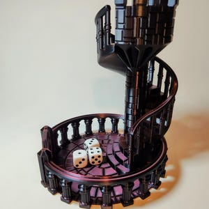 Puede incluir: Una torre de dados de color marrón oscuro impresa en 3D con forma de escalera de caracol con una pequeña torre en la parte superior. Tres dados blancos están en la plataforma de la torre.