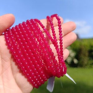 Könnte beinhalten: Eine Ansammlung mehrerer Stränge aus facettierten Edelsteinperlen in leuchtendem Fuchsia-Pink. Die Perlen sind rund und von einheitlicher Größe und zu langen, flexiblen Ketten aufgereiht, die eine reflektierende, polierte Oberfläche aufweisen.