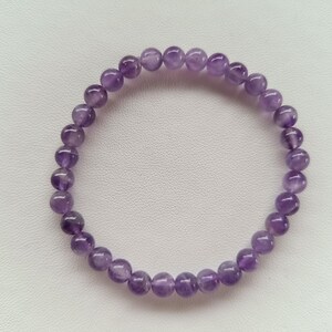 Könnte beinhalten: Ein Armband aus violetten Amethyst-Edelsteinen mit runden Perlen.