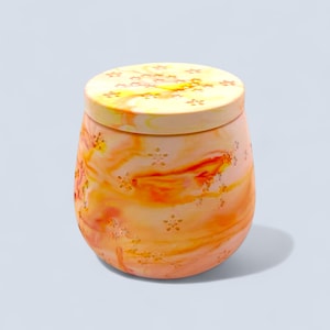 May include: A decorative jar with a lid, featuring a marbled design in shades of orange, yellow, and red. The jar has a rounded shape with small, flower-shaped cutouts. The lid also has a marbled pattern and flower cutouts.