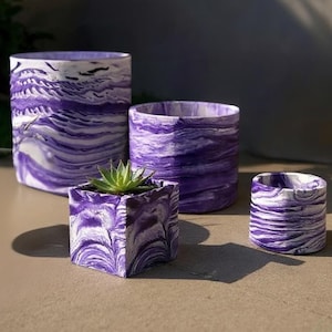 May include: Four plant pots in different sizes, with a marbled purple and white design. One square pot contains a small succulent. The other three are cylindrical, with a swirling pattern, ideal for indoor plants.