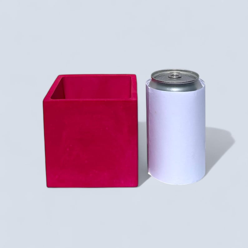 A handmade 10 cm square bright magenta plant pot, featuring a matching vibrant fuchsia interior. Perfect for small houseplants, succulents, and herbs, its compact size allows it to fit on desks, counters, and windowsills, adding a pop of color. It is slightly shorter and twice as wide as a nearby can for scale.
