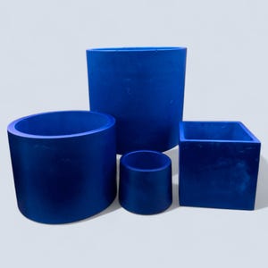 May include: A set of four cobalt blue planters in different shapes and sizes. The collection includes a cylindrical, a round, a square, and a small cylindrical planter. The planters are made of a solid material with a matte finish.