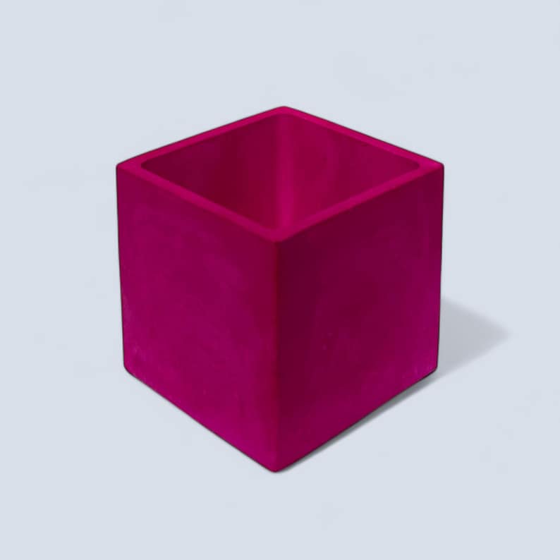 A handmade square 10 cm bright magenta plant pot. The interior of the pot can be seen and it boasts the same vibrant fuchsia colour as the exterior. The pot can hold small houseplants, succulents and herbs and its compact sized allows it to be placed anywhere from desks and counters to windowsills to bring a vibrant pop of colour.