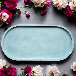 May include: A light blue oval-shaped concrete tray with a smooth surface. The tray is surrounded by pink and red roses.