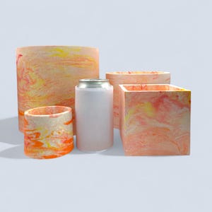 May include: A selection of decorative planters and a drinks can. The planters have a marbled design in orange, yellow, and white. The can is silver and white. The planters are cylindrical and square.