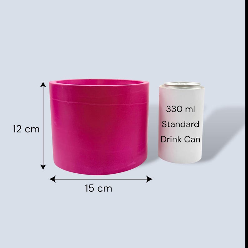 Bright fuchsia round plant pot with measurement arrows showing 12 cm height and 15 cm width, placed beside a standard 330 ml drinks can for size comparison on a pale grey background.