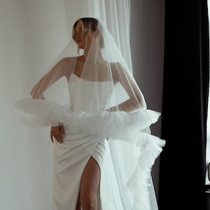 May include: A white wedding dress with a long, flowing skirt and a high split. The dress has a strapless bodice and a veil with a ruffled trim. The model is wearing white heels. The text "ToshaShop" is visible in the bottom centre of the image.