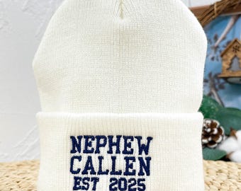 Può includere: Berretto di lana bianco con ricamo blu che dice "Nephew Callen Est 2025".