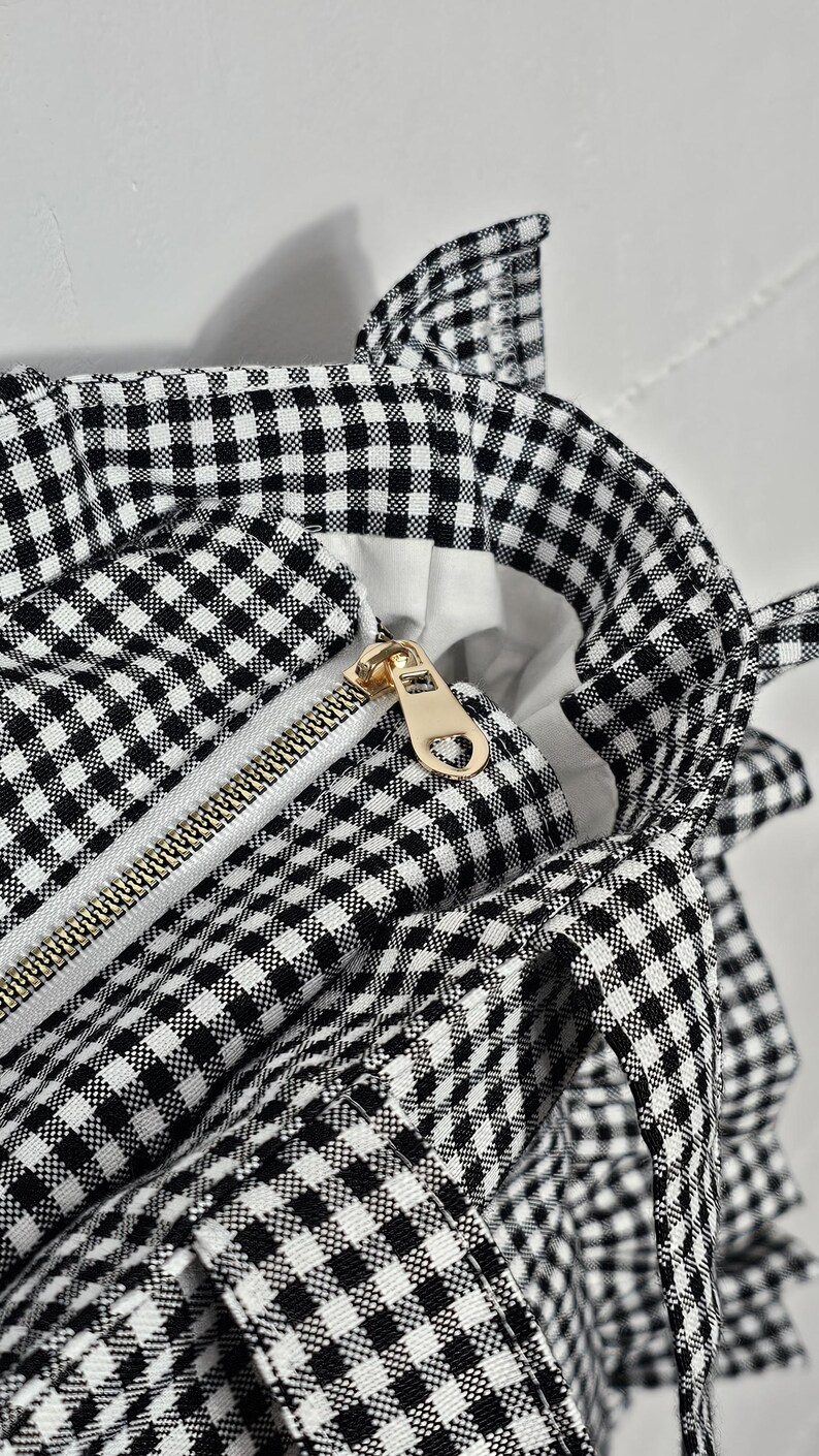 May include: Close-up of a black and white gingham tote bag. The bag features a gold zipper and a white interior. The bag has a classic checkered pattern and is a stylish accessory.