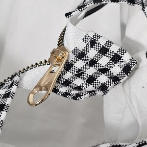 May include: Close-up of a gold zipper on a white and black checkered fabric. The zipper is partially open, revealing a white interior. The fabric has a classic gingham pattern.